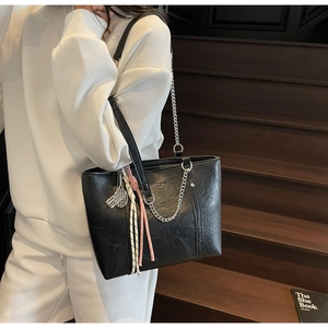 Detail of black pleated tote bag with silver chain and tennis racket charms accessory
