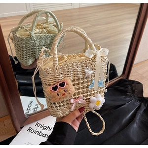 Detail of woven straw bucket bag featuring cute teddy bear, bows, and drawstring lining