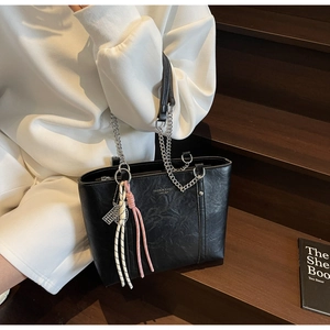 Detail of black leather tote bag with silver chain strap and colorful cord charms