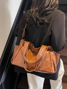 Brown high-gloss faux leather tote bag with long strap shown on a person on stairs