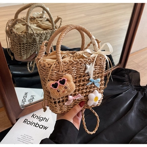 Detail of woven straw bucket bag with cute bear and bow charms on soft satin