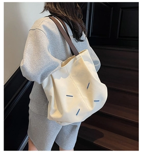 Detail view of large canvas tote bag featuring four white stitches and leather straps