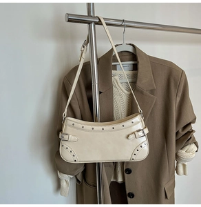 Détail d'un sac à bandoulière crème à rivets sur cintre avec une tenue chic et décontractée
