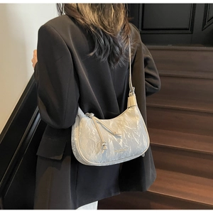 Detailed close-up of crescent shoulder bag with silver crinkled texture and metal ball drawstring
