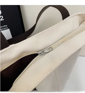 Detailed close-up of the smooth silver metal zipper on the cream canvas tote bag