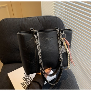 Close-up of black lychee leather tote bag with chain strap and tennis racket pendant