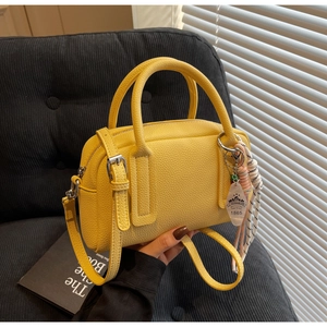 Detail of yellow lychee leather mini Boston bag with outdoor life tag and woven charms
