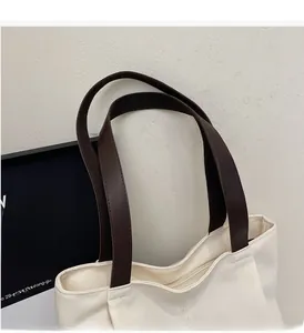 Close-up of durable brown leather handles and stitching on an off-white canvas tote bag