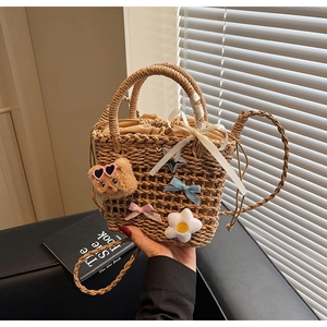Detail of woven straw bucket bag with plush bear, floral charms and drawstring lining