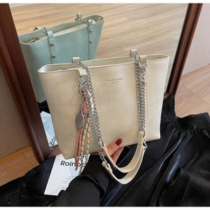 Detail of cream tote bag featuring textured leather, silver chain strap, and tassel charm