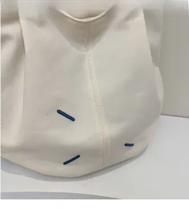 Close-up of cream canvas tote bag showing soft texture and blue embroidery details