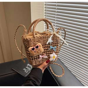 Detail of woven straw bucket bag with plush bear charm and drawstring closure