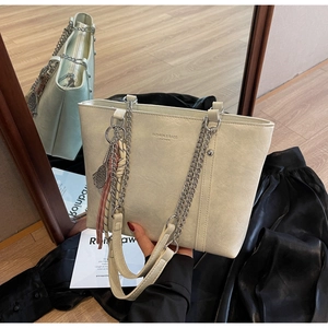 Detail of cream white tote bag featuring metallic chain strap and engraved brand lettering