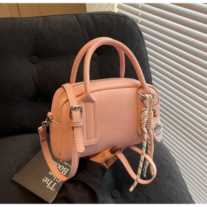 Pink lychee texture leather boston bag with stylish charm on a grey sofa background