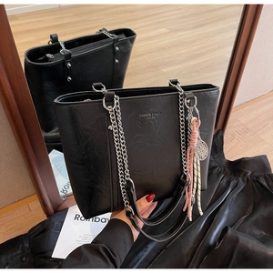 Detail of black pebbled leather tote bag with gold logo, chain strap and tassels
