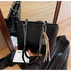 Close-up of black leather tote bag with chain strap and tennis racket metal pendant
