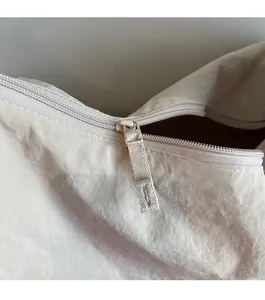 Detailed close-up of smooth metal zipper and fabric puller on cream canvas tote bag