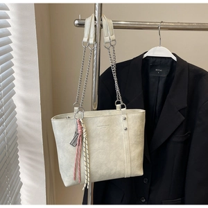 Detailed close-up of cream leather tote bag featuring fashion text and hanging charm decor
