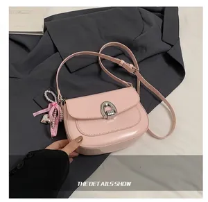 Détail du sac selle en cuir verni rose avec boucle en U argentée et breloque en perle