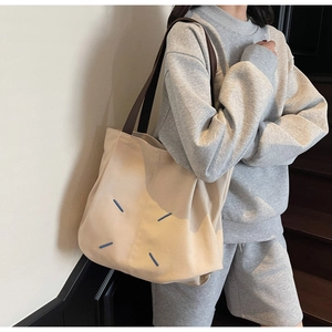 Detail of a beige canvas tote bag featuring signature blue stitching and brown leather straps