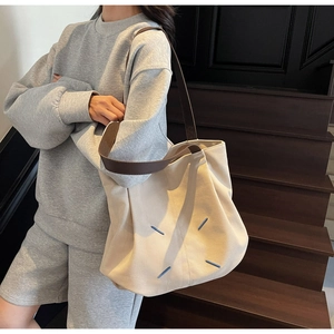 Detail of beige canvas tote bag with brown faux leather straps and signature four corner stitches