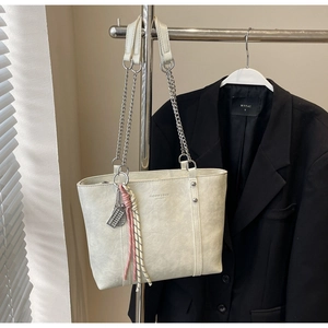 Close-up of cream leather tote bag with embossed fashion text and chain handle detail