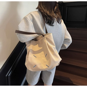 Detailed back view of a beige canvas tote bag with blue stitching and brown shoulder strap