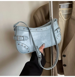 Détail du sac baguette bleu clair avec clous argentés et bandoulière sur fond de vêtements