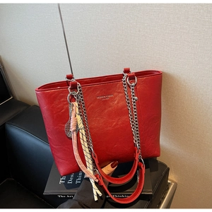 Close-up of red lychee leather tote bag featuring silver chain and tennis racket charm