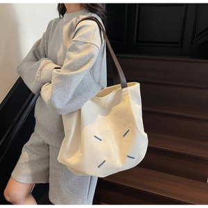 Detail of minimalist canvas tote with contrast brown leather straps and blue accent stitching
