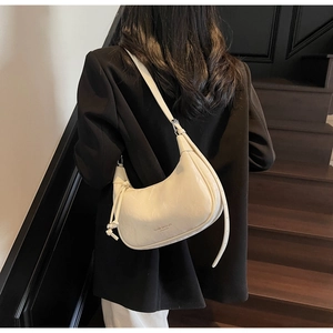 Close-up of a cream crescent bag with gathered texture and adjustable strap on stairs