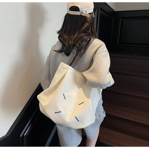Detail view of white canvas tote bag featuring iconic blue four-corner stitch design