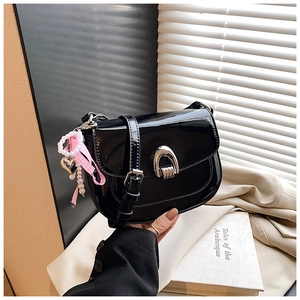 Gros plan sur le sac selle en cuir verni noir avec boucle fer à cheval argenté et ruban rose
