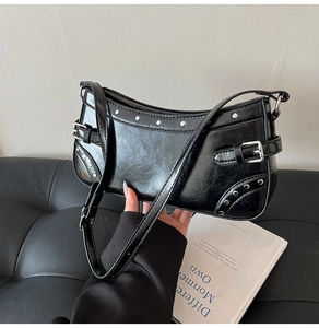 Détail du sac sous le bras noir avec rivets argentés et boucles sur un canapé