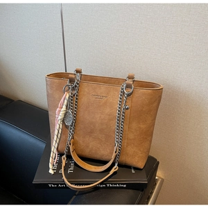 Close-up of vintage brown leather tote bag with metal chain strap and decorative charms