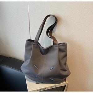 Detailed view of grey canvas tote bag with brown leather handles and blue corner stitching