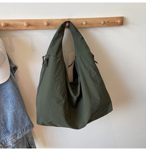 Detail of dark green waterproof nylon tote bag featuring a side zipper pocket and wide strap