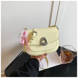Détail d'un sac selle en cuir verni jaune clair avec breloques perles et ruban