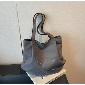 Detail of dark grey canvas tote bag featuring brown leather handles and blue accent stitching
