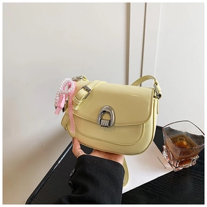 Détail du sac selle en cuir verni crème avec boucle argentée et breloque en perles