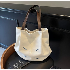 Detailed close-up of off-white canvas tote bag with brown leather handles and blue stitching