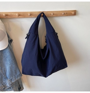 Close-up of navy blue oversized nylon tote bag with textured surface on wooden wall hook