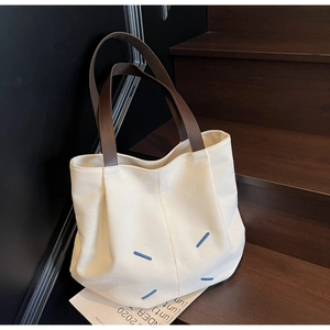 Detail of beige canvas tote bag with iconic four blue diagonal stitches on wood stairs