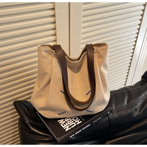Detailed close-up of large canvas tote bag with brown leather handles and blue accent stitching