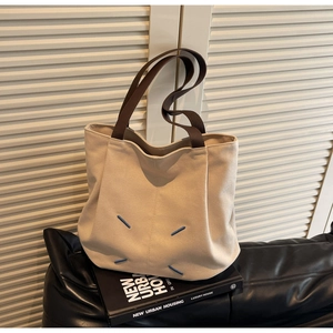 Detail of off-white canvas tote bag with dark brown straps and iconic four blue stitches