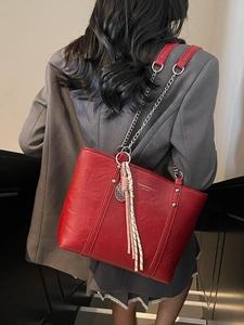 Red faux leather tote bag with chain strap and tassel charm shown on shoulder
