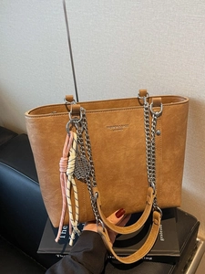 Brown vintage faux leather tote bag with chain strap and tennis racket charm on leather seat
