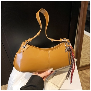 Close-up of ginger yellow crescent underarm bag with fringe and glossy PU leather finish