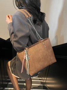 Brown leather tote bag with metal chains and rivets shown on model in a modern interior