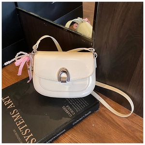 Détail du sac selle en cuir verni crème avec boucle argentée et breloque en perles